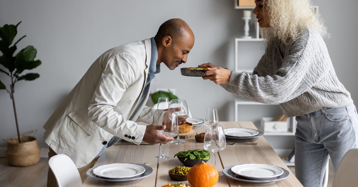 How do I soften home made Split Pea with crunchy Peas? - Side view of African American man smelling fresh meal while standing at served table with dishware and food with black wife