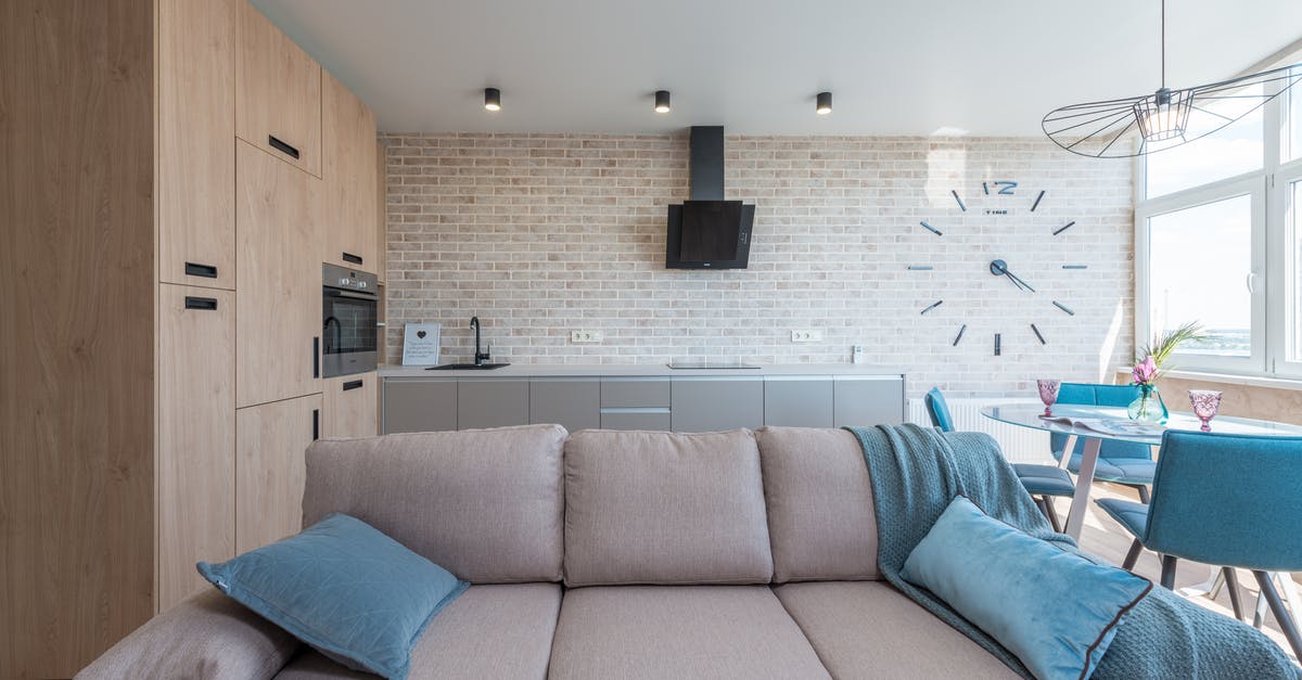 How do I use the clock on my Ilve oven? - Minimalistic interior design of modern light studio consisting of big sofa and kitchen with dining table and chairs against brick wall in daylight