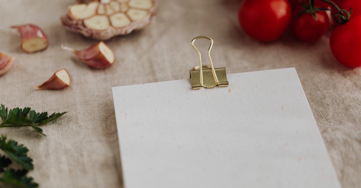 How do restaurants chop up garlic? - From above of empty clipboard for recipe ingredients or menu placement located on desk with linen tablecloth and surrounded by fresh delicious tomato on branch together with chopped garlic and green parsley