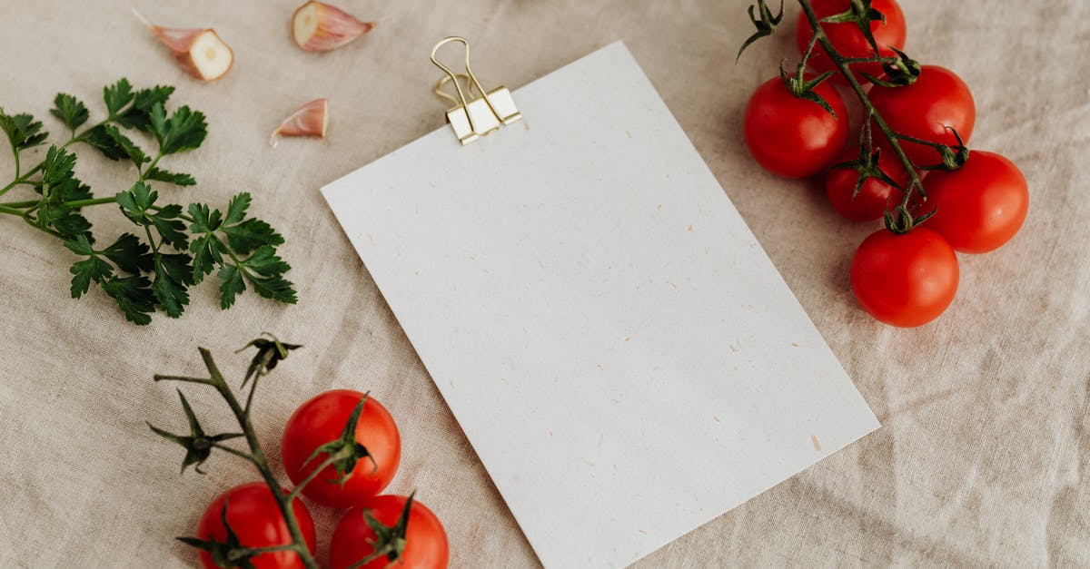 How do restaurants chop up garlic? - Top view of blank clipboard with golden paper binder placed on linen tablecloth among tasty red tomatoes on branches together with chopped garlic head and green parsley ideal for recipe or menu