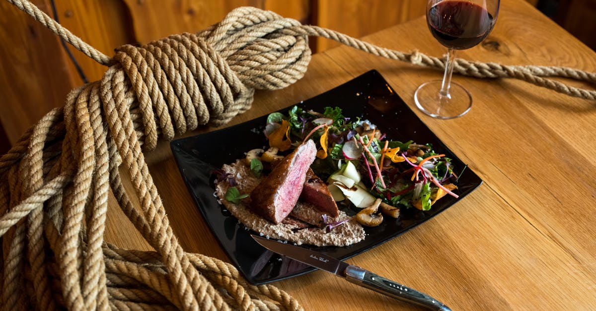 How do they Prepare Steak so fast in Restaurants? - From above of ceramic plate with beef steak pieces topped on mushroom sauce and vegetable salad served with knife and glass of red wine placed on wooden table with rope tied in knot