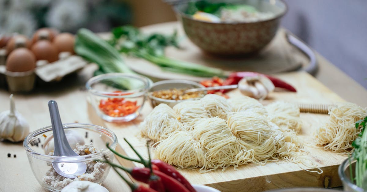 How do you cook flavored pasta? - Composition of uncooked noodles on wooden board near fresh various vegetables and eggs arranged on table in kitchen before cooking Asian noodles soup