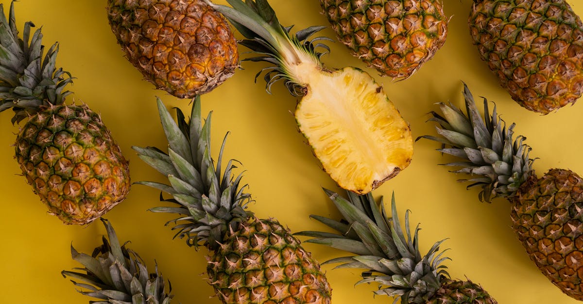 How do you cut/process a whole pineapple? - Top view composition of fresh pineapples with juicy colorful flesh placed on yellow background in light studio during ripening season