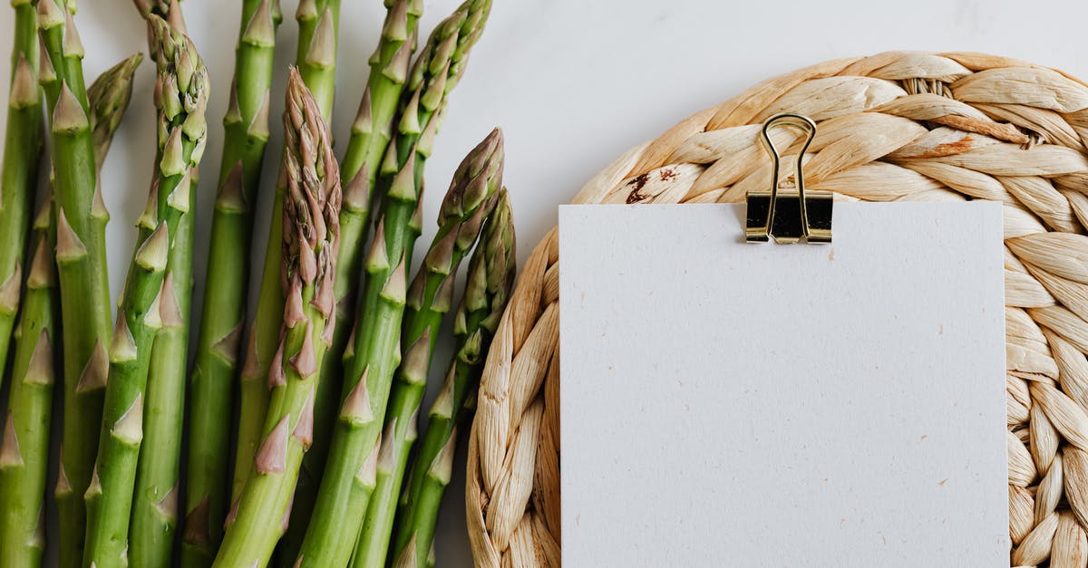 How do you organize your recipes? - Top view of asparagus pods with sheets of paper fastened by paper clip on white desktop