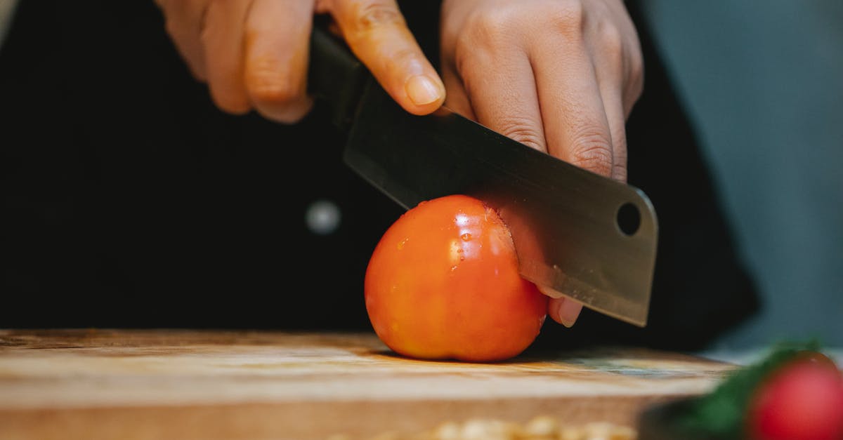 How do you properly clean a cutting board and knife to prevent cross contamination? - Chef cutting tomato with knife on wooden cutting board