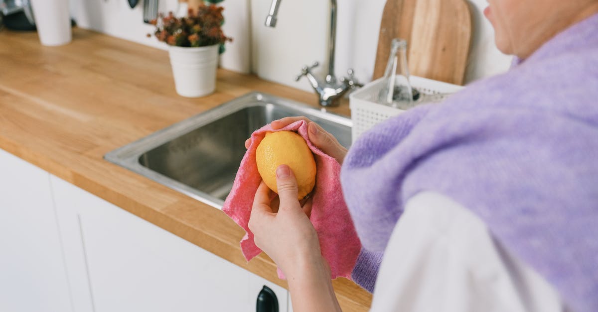 How do you properly wash hands after dealing with raw chicken? - Crop unrecognizable person in casual clothes standing and wiping ripe fresh lemon with cloth in light kitchen in daytime