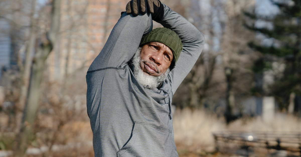 How do you raise your dough in cold seasons? - African American male with white beard in cap looking at camera in park while warming up with raised arms in gloves
