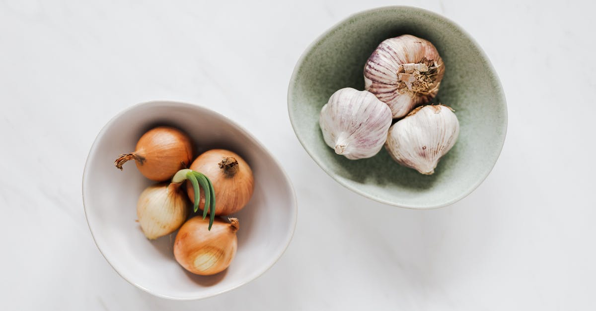 How do you remove garlic smells from your fingers? - Top view of unpeeled raw yellow onion in white bowl and unpeeled raw aromatic garlic in light green bowl placed on marble table