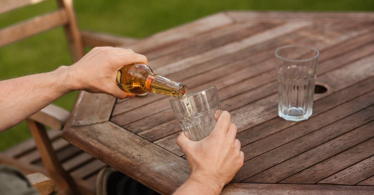 How do you thicken a cold filling? - From above crop anonymous male sitting at wooden table and pouring cold beer into glass cup at weekend in yard