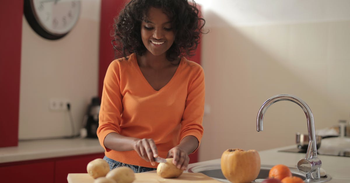 How do you wash fruit and veggies effectively? - Cheerful woman cutting potatoes in kitchen