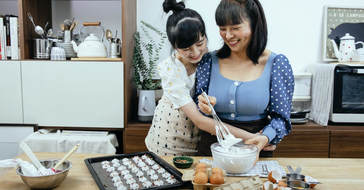 How does a splash of vinegar help when poaching eggs? - Happy Asian mother and daughter cuddling while preparing meringues in kitchen