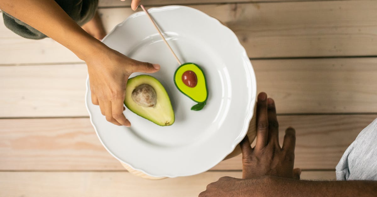 How does imitation cinnamon flavor differ from real? - Top view of crop anonymous African American people near white plate with half of ripe avocado and sweet lollipop with similar shape