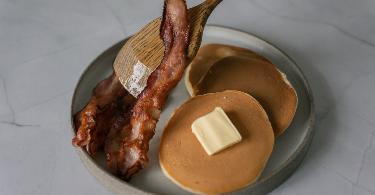 How does substituting Butter for Margarine/Shortening affect the Recipe - High angle of delicious pancakes with butter piece near sliced fried bacon and wooden kitchen spatula on plate on white table in bright place
