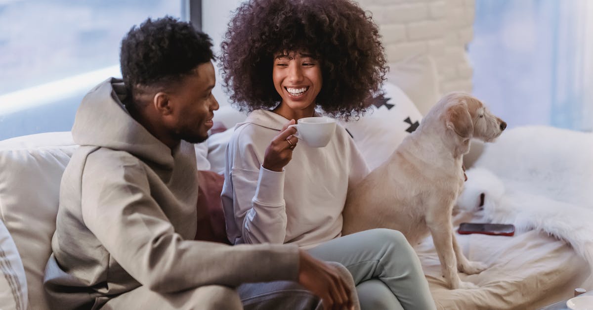 How does the addition of Chicory affect coffee? - Cheerful young African American couple in stylish hoodies communicating and drinking coffee while resting on comfortable couch with cute bed