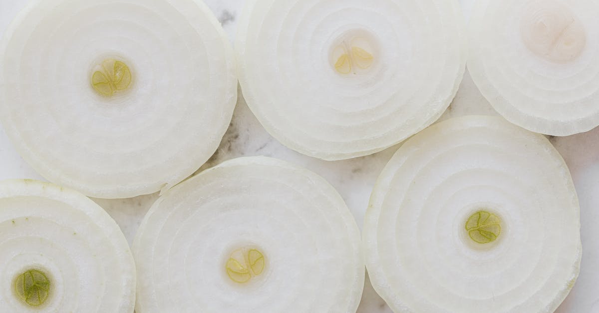 How does the way that I cut my garlic affect the taste of my food? - Top view closeup of ripe organic yellow peeled onion cut into rings and placed on white marble tabletop