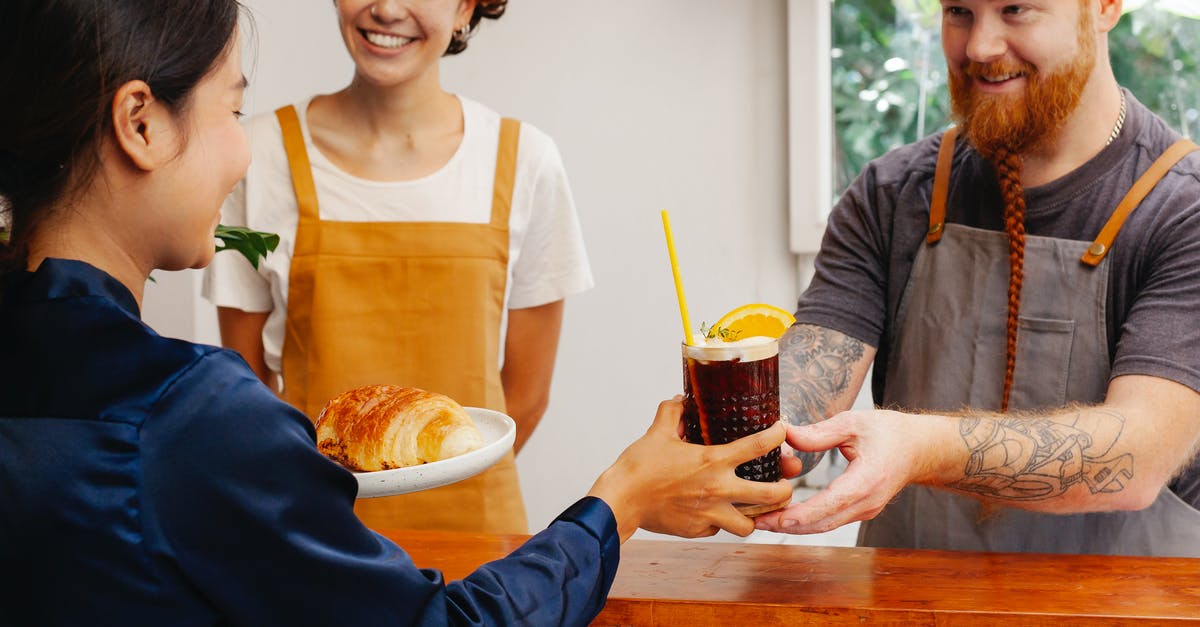 How does velveting work? - Crop cheerful workers passing tasty pastry and glass of alcoholic beverage to ethnic partner at counter