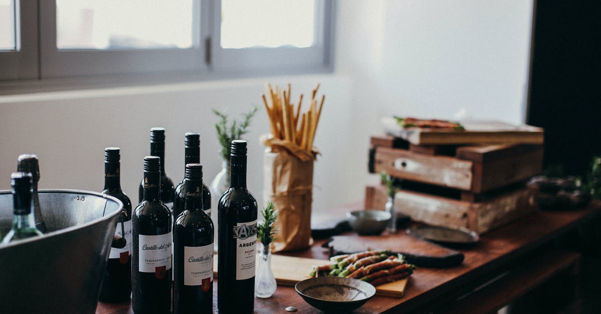 How Does Wine Enhance Flavor? - Various bottles of alcoholic drinks placed on table with grissini sticks and wooden boxes near green branches in vase in room