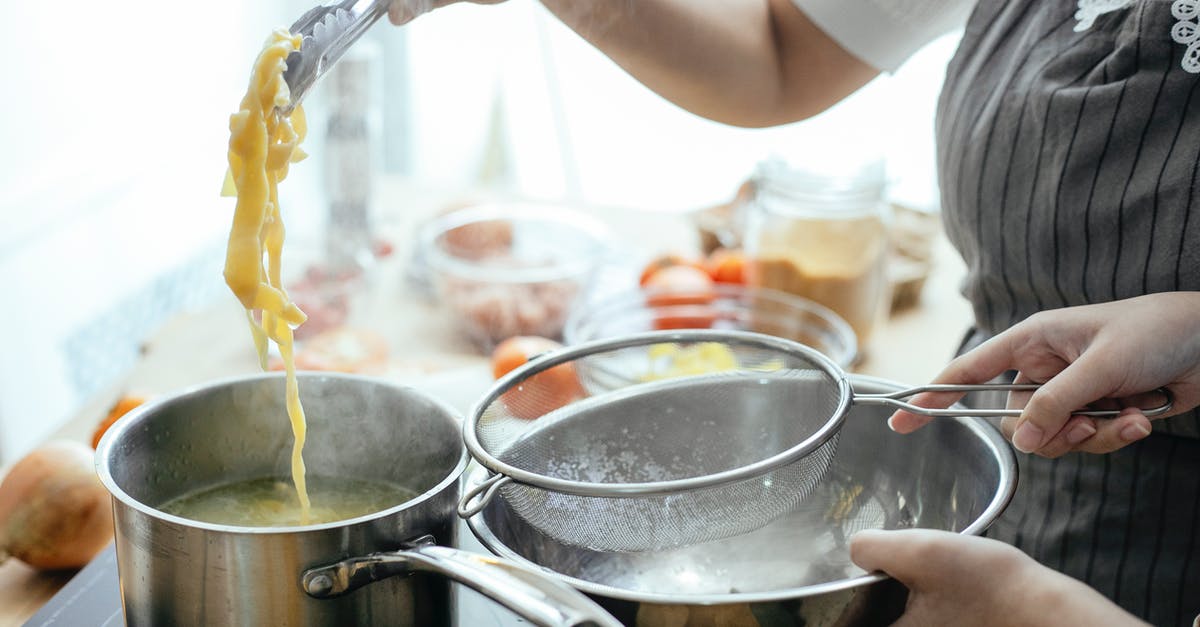 how early can I put food into a slow-cooker? - Unrecognizable cooks with strainer putting pasta out of pan with boiling water while standing near stove in kitchen on blurred background