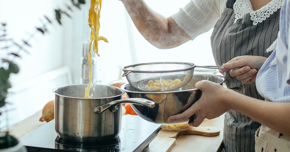 how early can I put food into a slow-cooker? - Unrecognizable female cooks putting pasta from pot into sieve while cooking lunch at table with stove in kitchen on blurred background