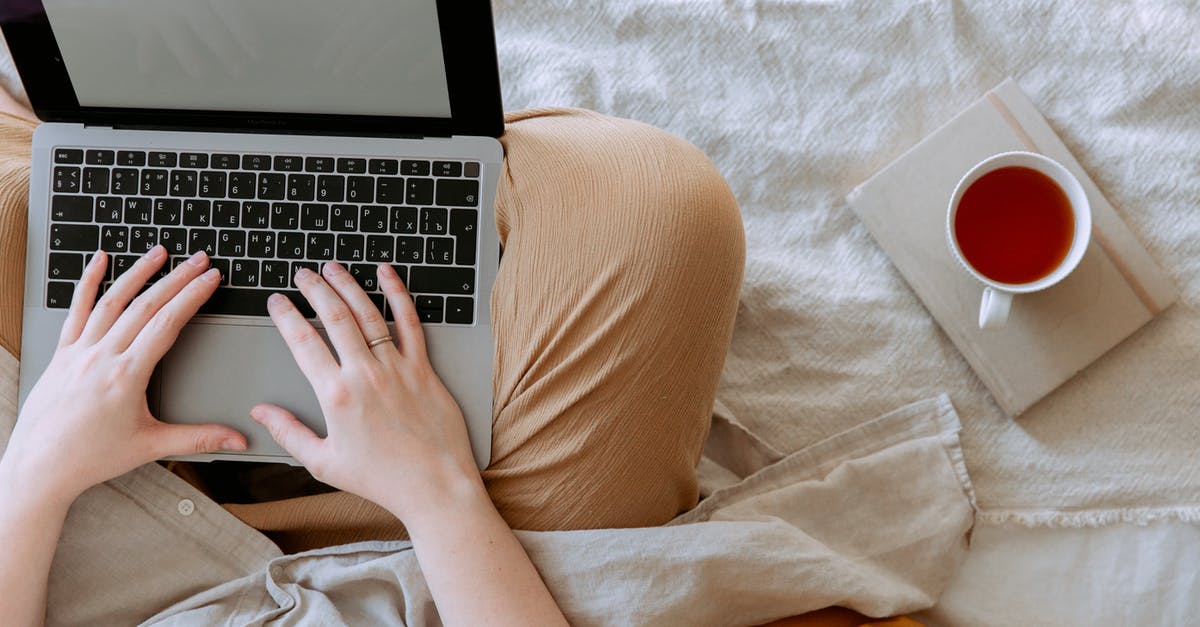 How is British tea prepared? - Top view anonymous remote worker typing on keyboard of laptop with blank screen while sitting with crossed legs on bed with tea aside at home