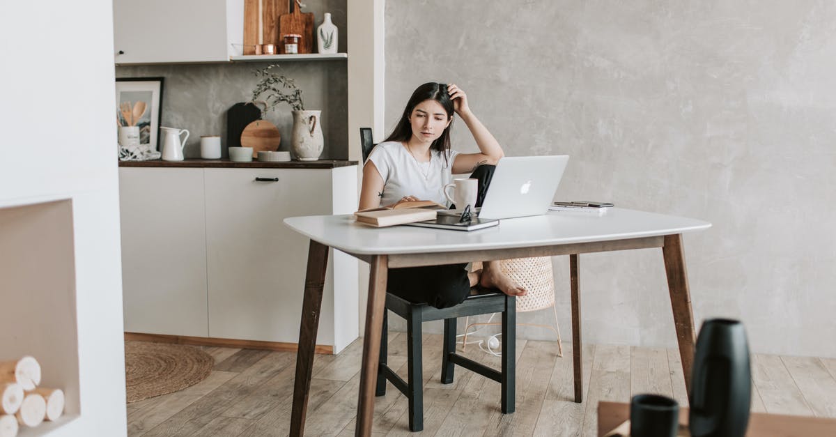 How is British tea prepared? - Concentrated female student sitting barefoot on chair at table with netbook and notebook while reading book during distance education in modern apartment with minimal interior in eco design