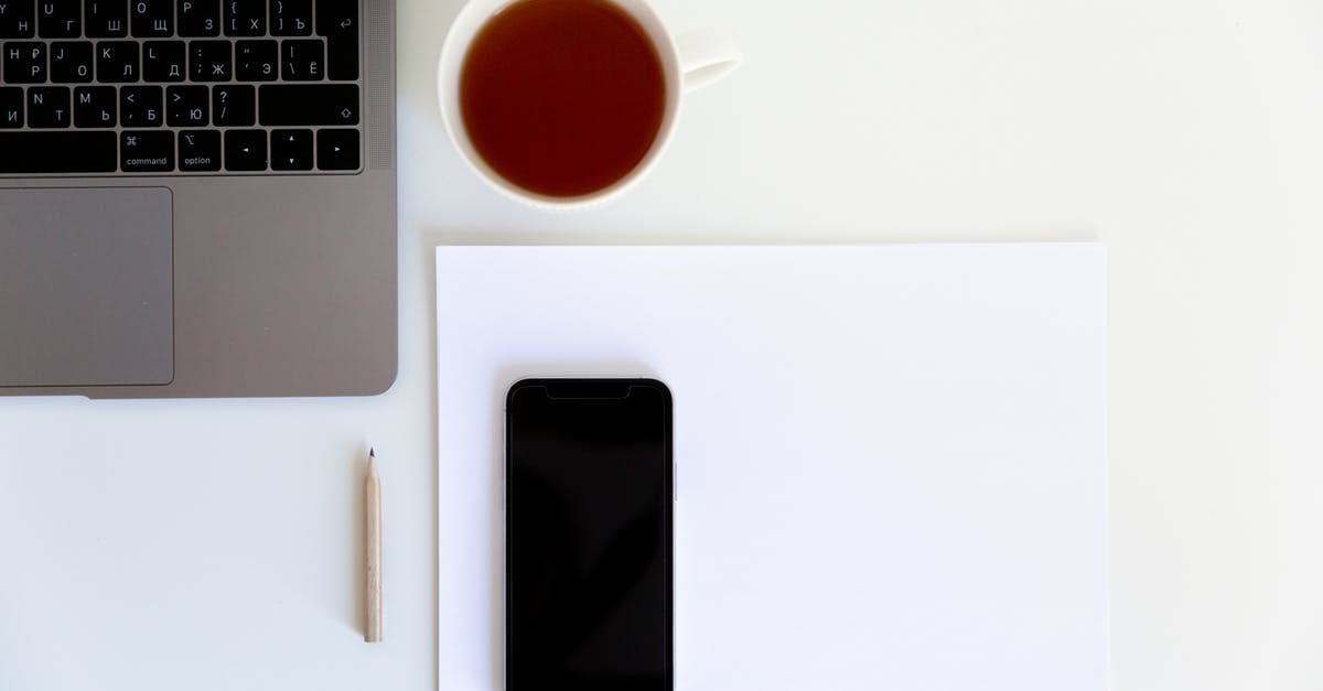 How is British tea prepared? - Workplace with smartphone placed on white paper with cup of tea aside near laptop and pencil