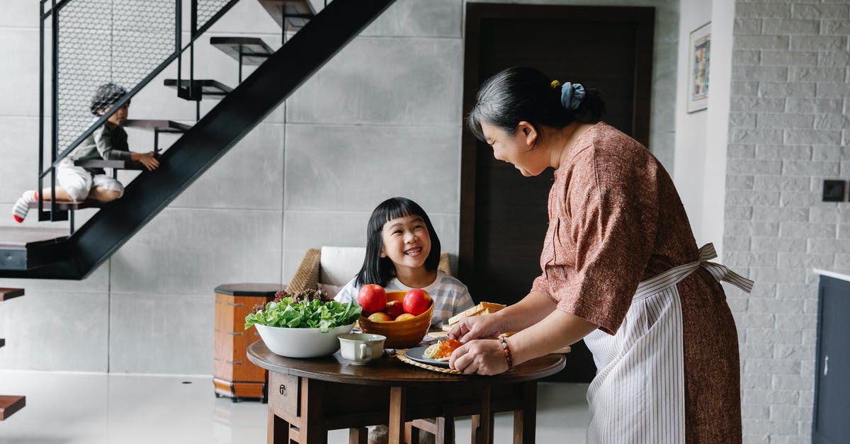 How is starch content of some vegetables reduced by cooking? - Cheerful little Asian girl sitting at table while grandmother serving lunch with fresh veggies