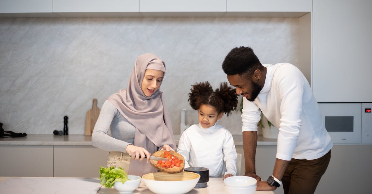 How is starch content of some vegetables reduced by cooking? - Delighted young diverse family standing near table in kitchen at home while cooking together at home