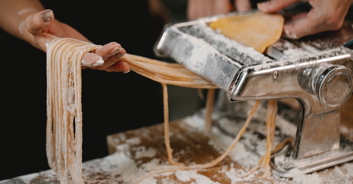 How long do I cook my brisket? - Crop anonymous female producing long noodle with metal pasta cutter on wooden table covered with flour