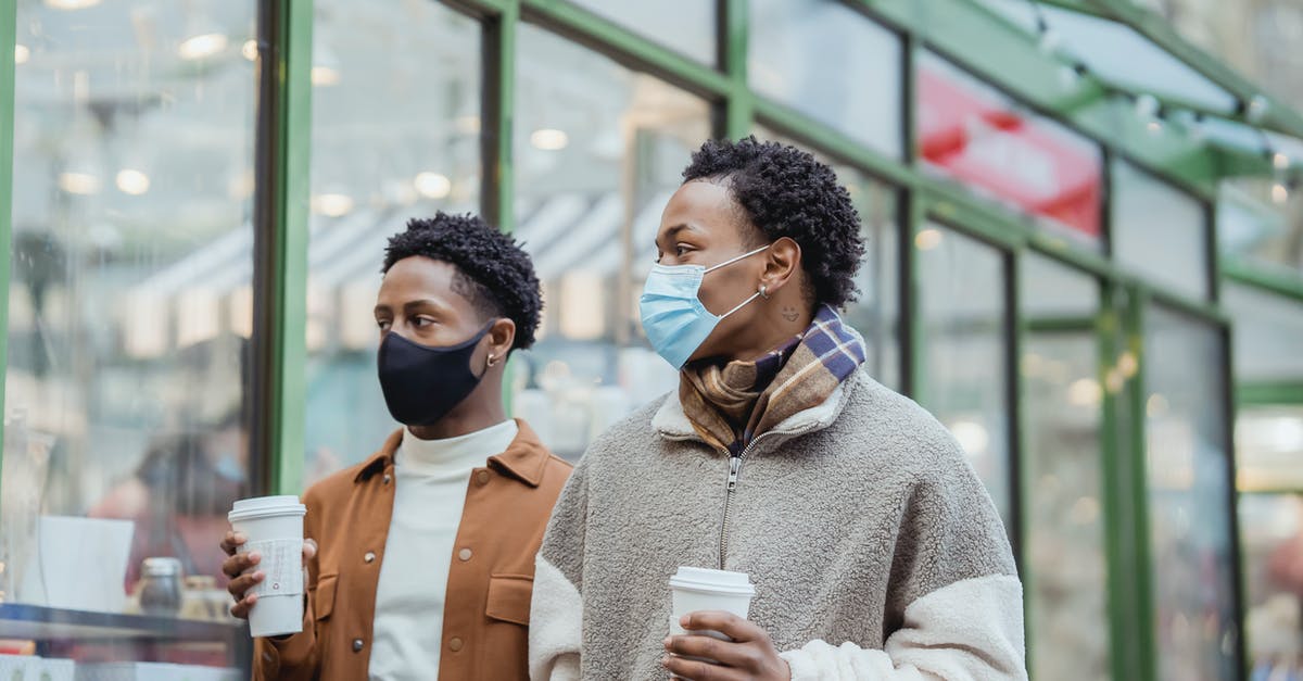 How long is coffee with creamer added safe in a thermos? - African American male couple in protective masks walking on street along building with paper cups of takeaway beverages in city