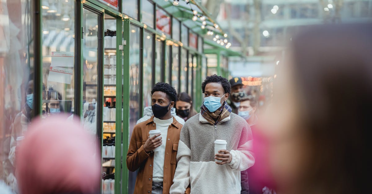 How long is coffee with creamer added safe in a thermos? - African American homosexual male in protective masks holding hands while strolling on street with takeaway coffee on street with people