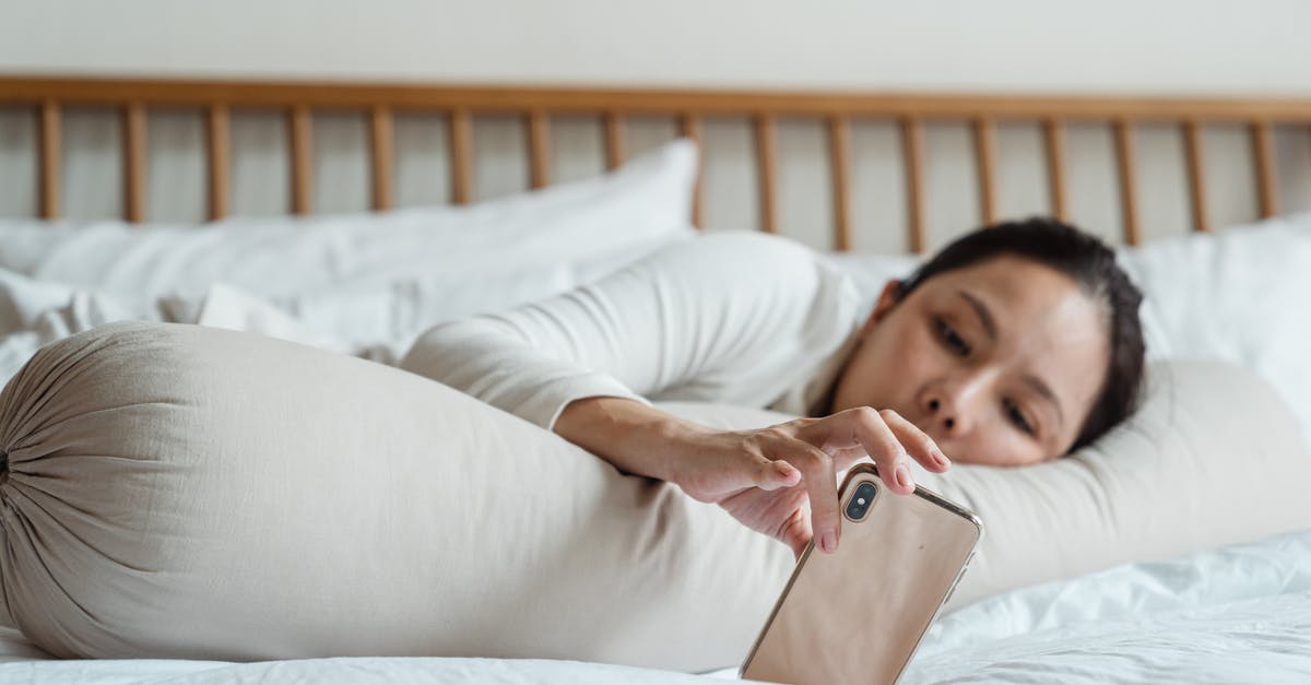 How long should I keep something in the freezer to chill it? - Content young ethnic female watching video on cellphone while lying on comfortable bed with long cylinder pillow in morning and enjoying free time