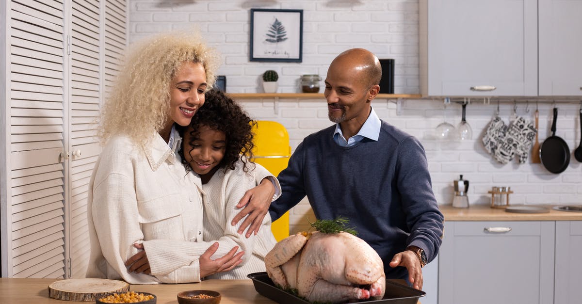 how long to cook a turkey per pound - Positive African American parents with daughter hugging while standing at table with raw turkey while cooking together in modern kitchen