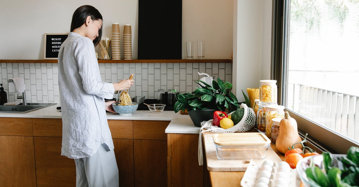 How long will homemade salad dressing stay good in the fridge? - Side view of young Asian female with long dark hair in comfy clothes preparing noodles while standing at counter with assorted fresh products in kitchen