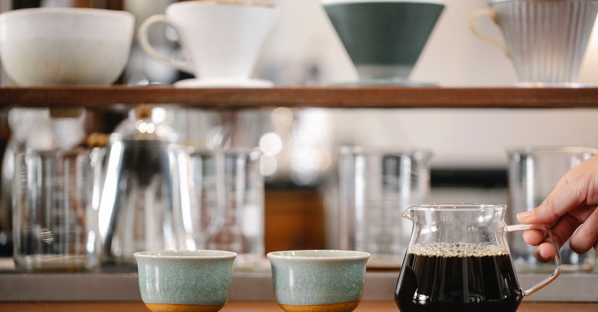 How many of this mug would be 750 grams of flour - Crop anonymous barista putting glass pot with coffee on table with cups near beakers and drippers on blurred background in modern cafe