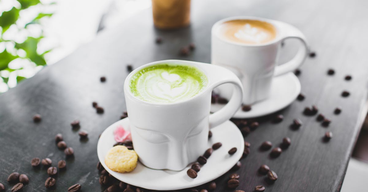 How much caffeine is in matcha powder? - From above of refreshing tasty matcha green tea latte and cappuccino in creative face shaped mugs placed on wooden table with scattered coffee beans