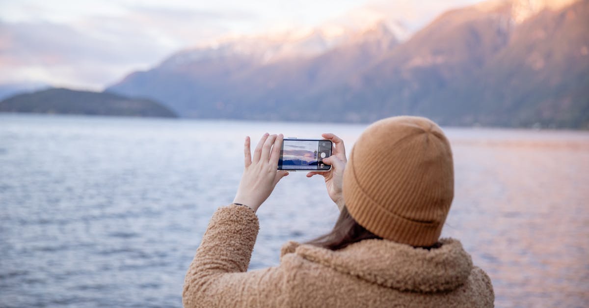 How much CO2 does it take to carbonate water using a household Soda Siphon? - Back view of unrecognizable female tourist in warm coat and hat taking photo on smartphone while standing on coast near water and enjoying seascape during trip