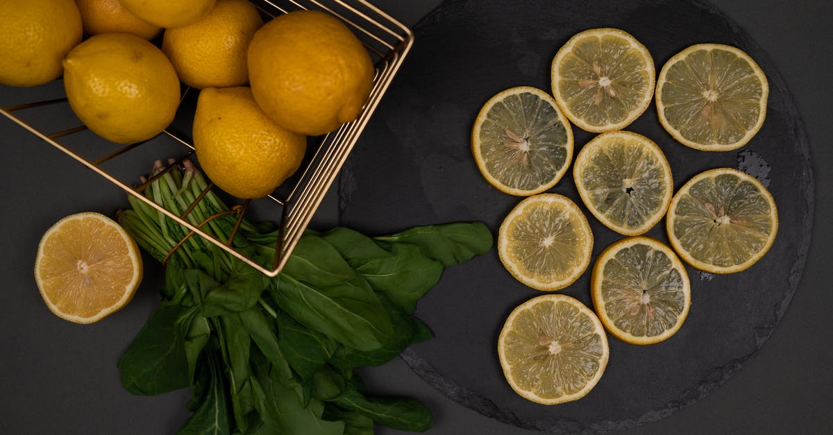 How much is a bunch of spinach? - Top view of fresh whole and cut lemons on black chopping board near spinach foliage on dark background