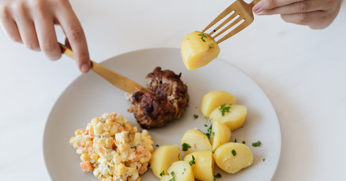 How much meat should I serve per person? - From above of crop anonymous person with cutleries eating delicious fried cutlet and hot boiled potatoes with parsley garnished with nutritious Russian salad