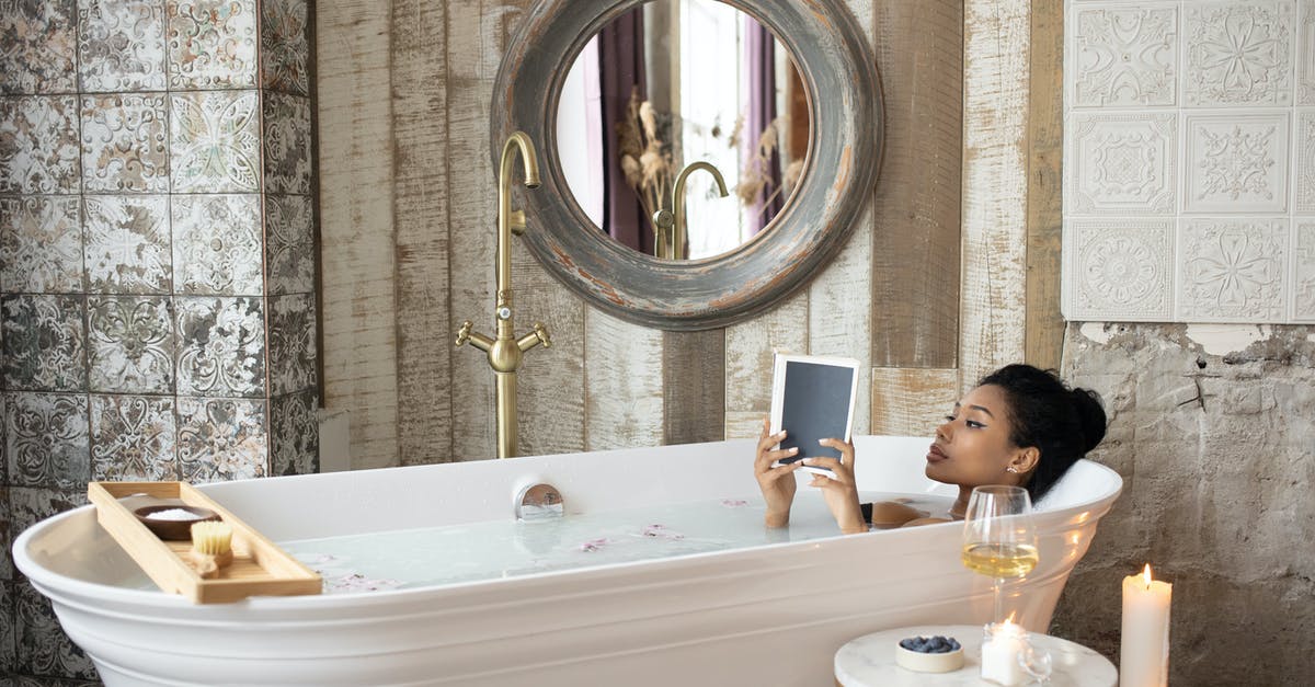 How much salt, add to tap water to purge bivalvia? - Young African American female reading book while taking bath in light bathroom with burning aromatic candles placed near round table with wineglass and berries on background of shabby stone walls