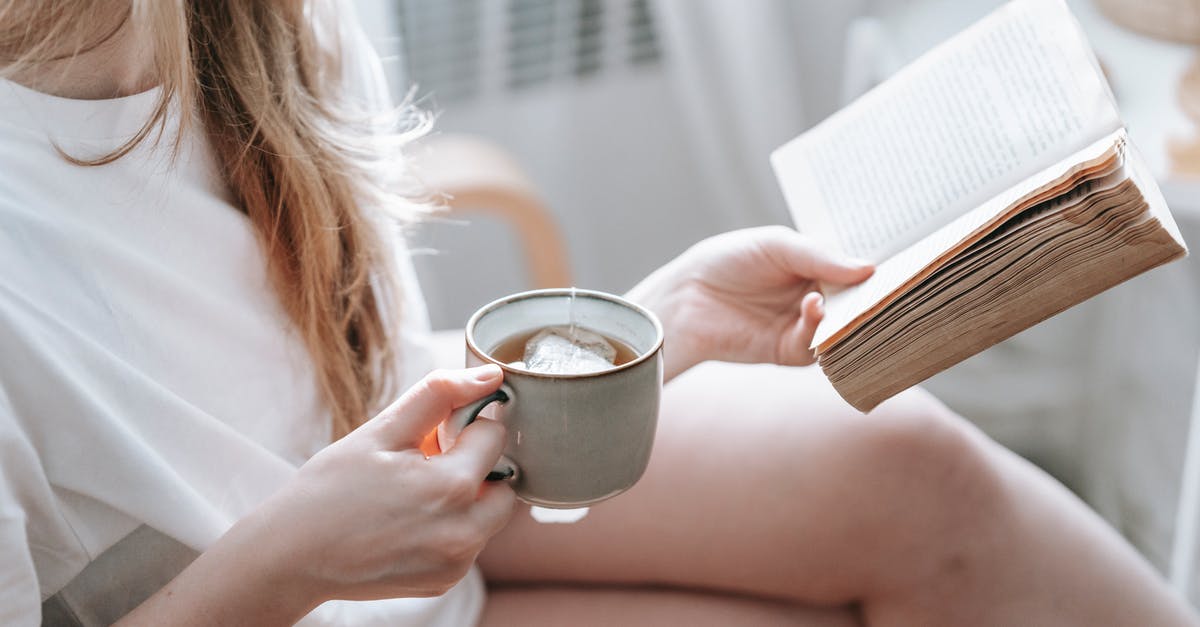 How much tea is ideal out of one tea bag? - Crop anonymous female with crossed legs and cup of hot drink reading aged textbook in armchair at home