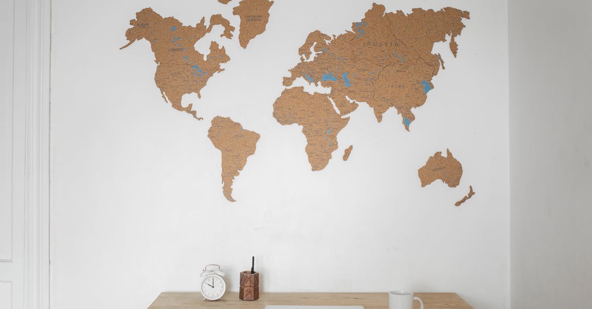 How should glasses/cups be oriented in storage? - Alarm clock near pen container with cup and laptop on table placed near silhouettes of world map on wall