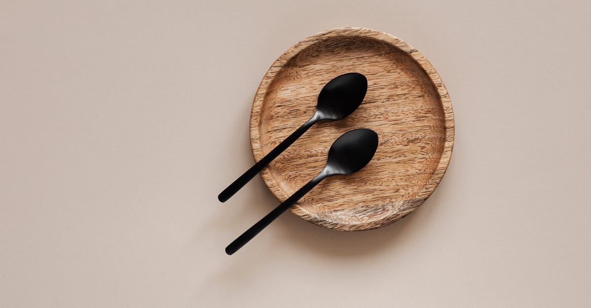 How should I clean my metal mesh tea strainer? - Top view of composition of round wooden plate with smooth surface and similar black metal spoons on beige surface