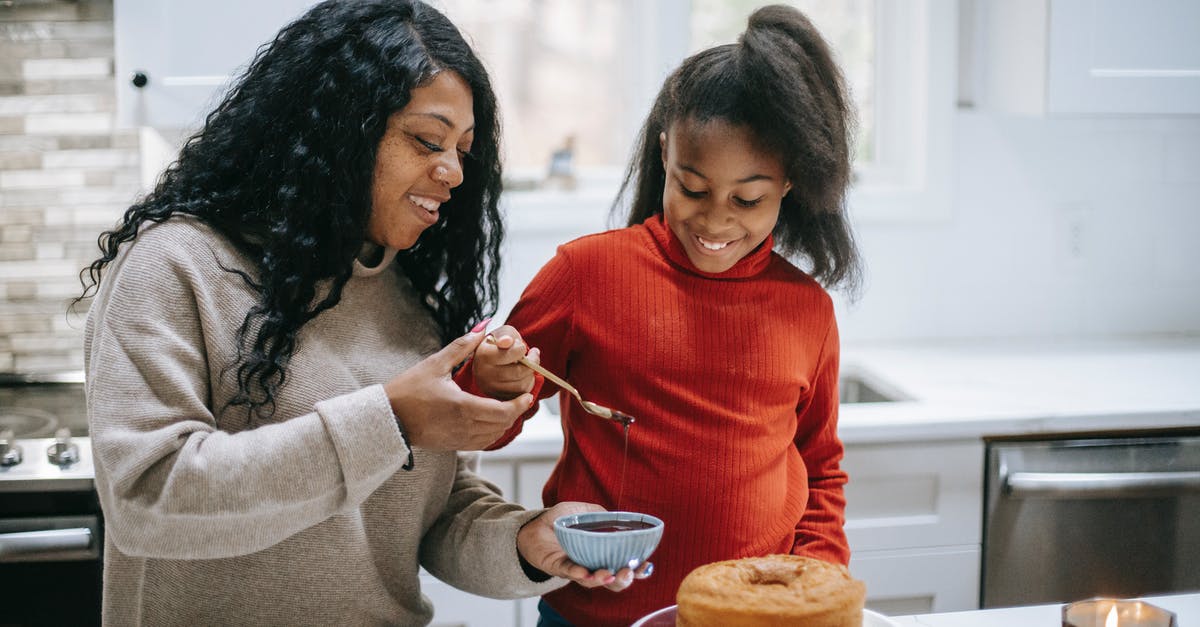 How should I convert my Victoria sponge to a chocolate sponge? - Young content black woman with girl decorating yummy sponge cake with chocolate glaze during New Year holiday