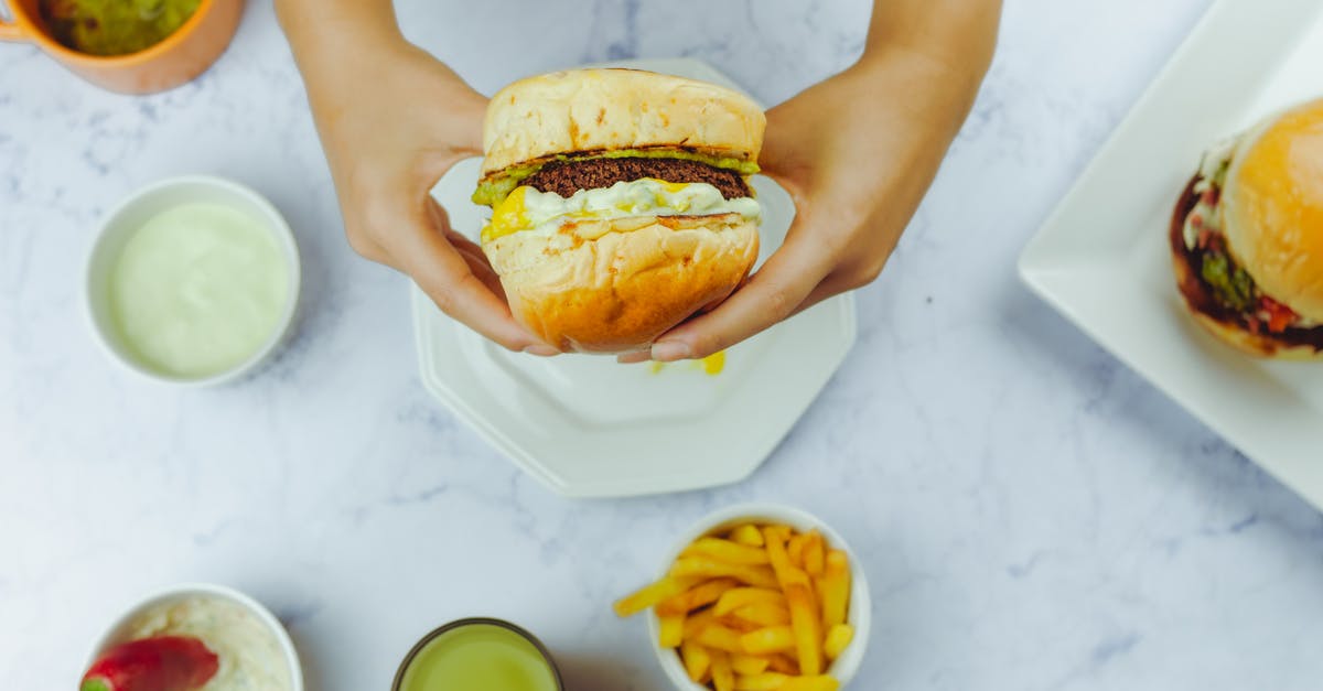 How should I cook a ham bone for chili? - Crop faceless person holding appetizing hamburger over table with fried potato and various sauce with red pepper