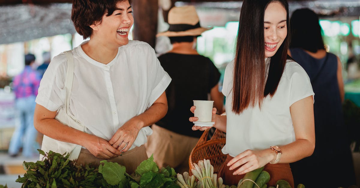 How should I store herb butter? - Cheerful Asian female friends picking fresh exotic greenery at oriental street store while laughing together