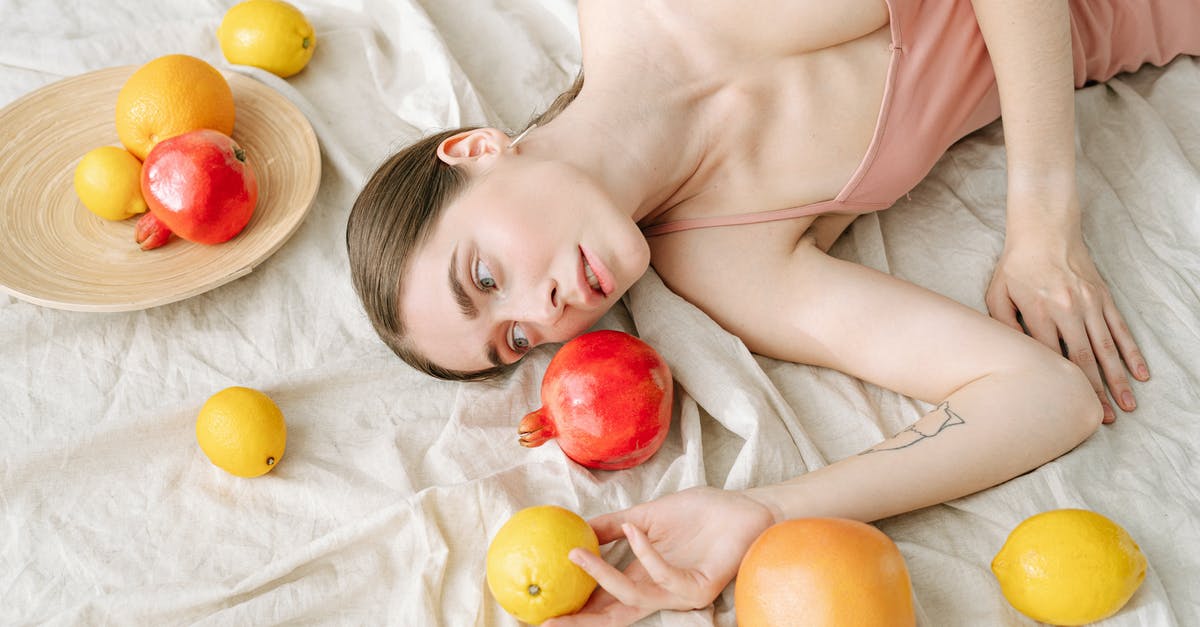 How should pomegranates be stored? - Woman in Pink Spaghetti Strap Dress Lying on White Linen Beside Fruits