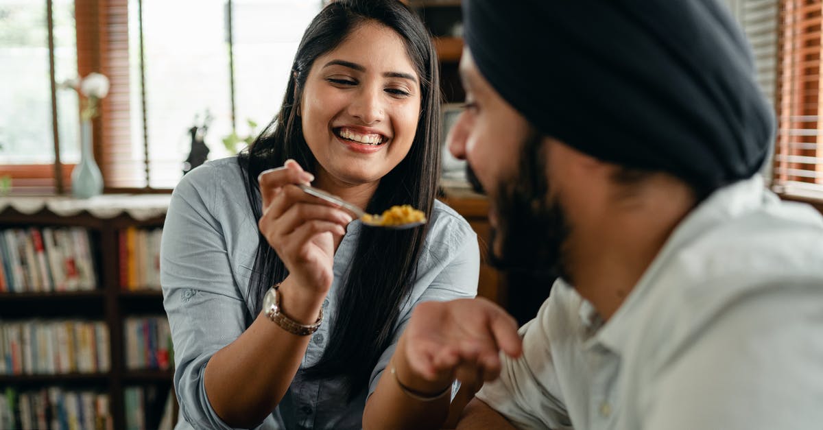 How spicy is authentic, traditional Palak paneer? - Happy young Indian woman smiling and feeding positive hungry boyfriend with delicious saffron rice