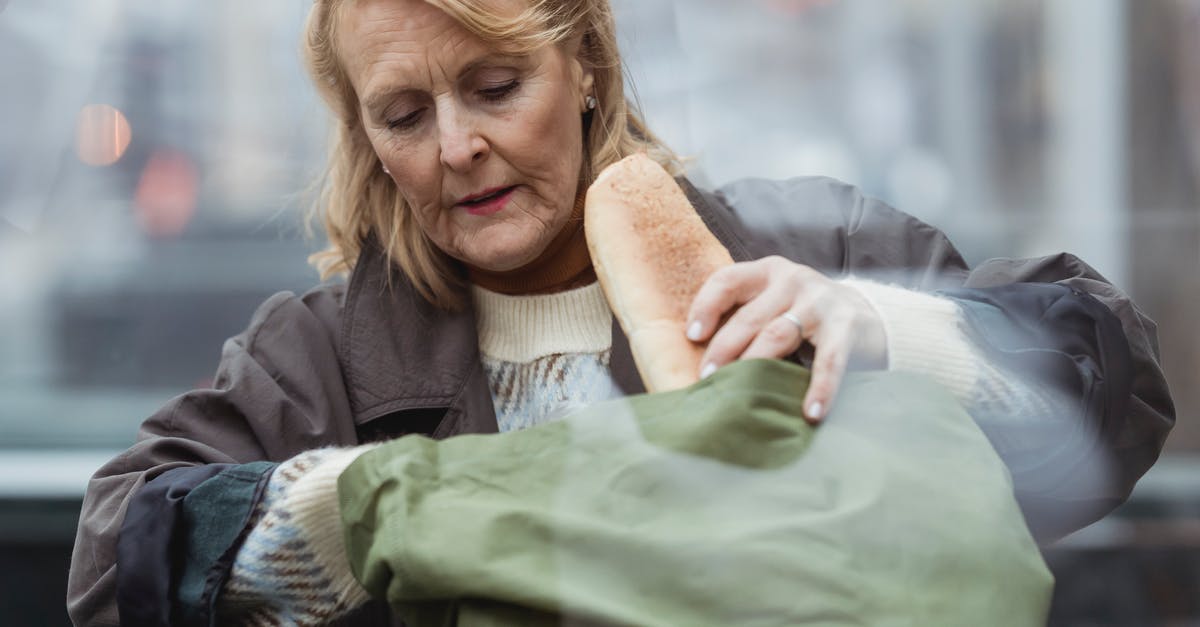 How to achieve great baguette crusts - Through glass view of senior female with wrinkled skin in warm clothes putting long loaf in textile bag in daytime