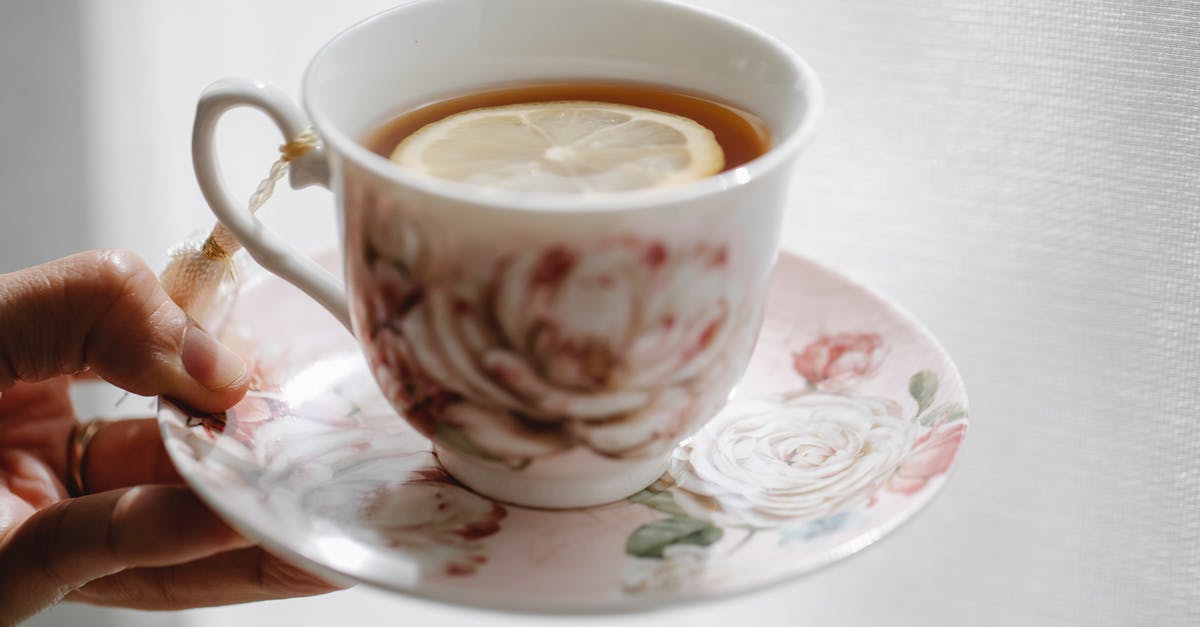 How to add lemon flavor to tea? - Hand of crop anonymous person holding elegant saucer with cup of hot aromatic tea with slice of lemon